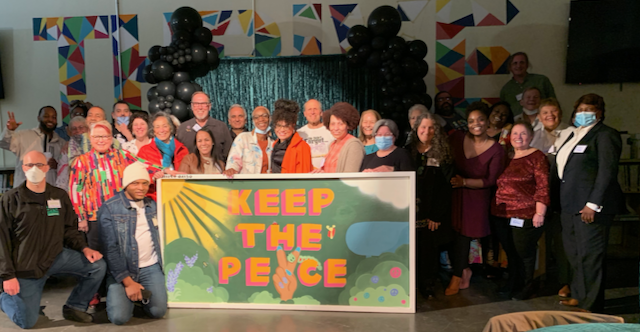 Alumni, students, teachers, and friends of Greater Egleston High School, a co-founder of the Egleston Square Peace Garden, hold up a painting entitled "Keep the Peace" to show their support.